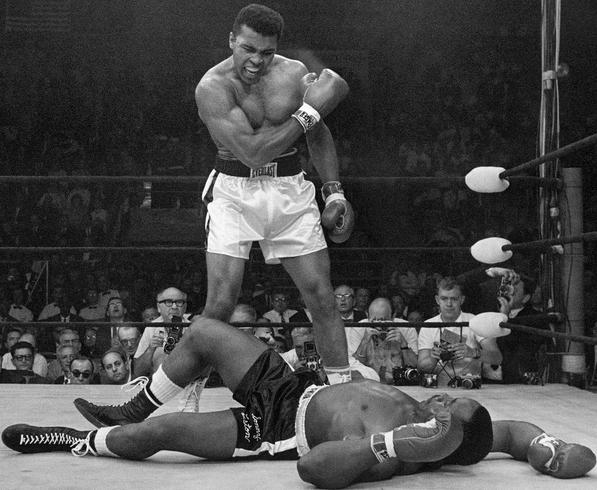 Muhammad Ali stands over a fallen Sonny Liston in the boxing ring, gesturing and shouting down at him during their 1965 rematch.