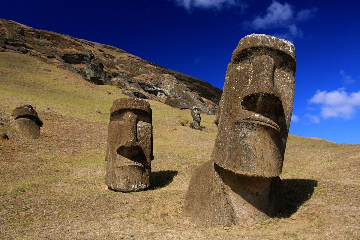 Row of large stone moai statues standing on the grassy slopes of the Rano Raraku quarry on Easter Island.