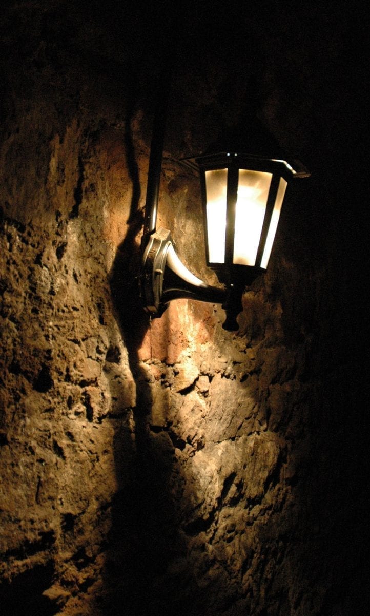 A bare stone chamber inside the Edinburgh Vaults beneath South Bridge, its rough masonry walls and low arched ceiling lit dimly in the underground dark.