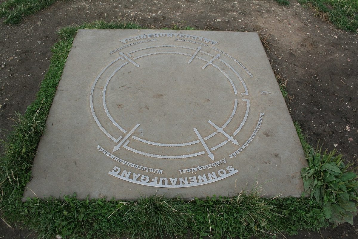 Reconstructed rings of tall wooden palisade posts of the Goseck Circle Neolithic enclosure, with gate gaps, standing under a cloudy sky in Saxony-Anhalt, Germany