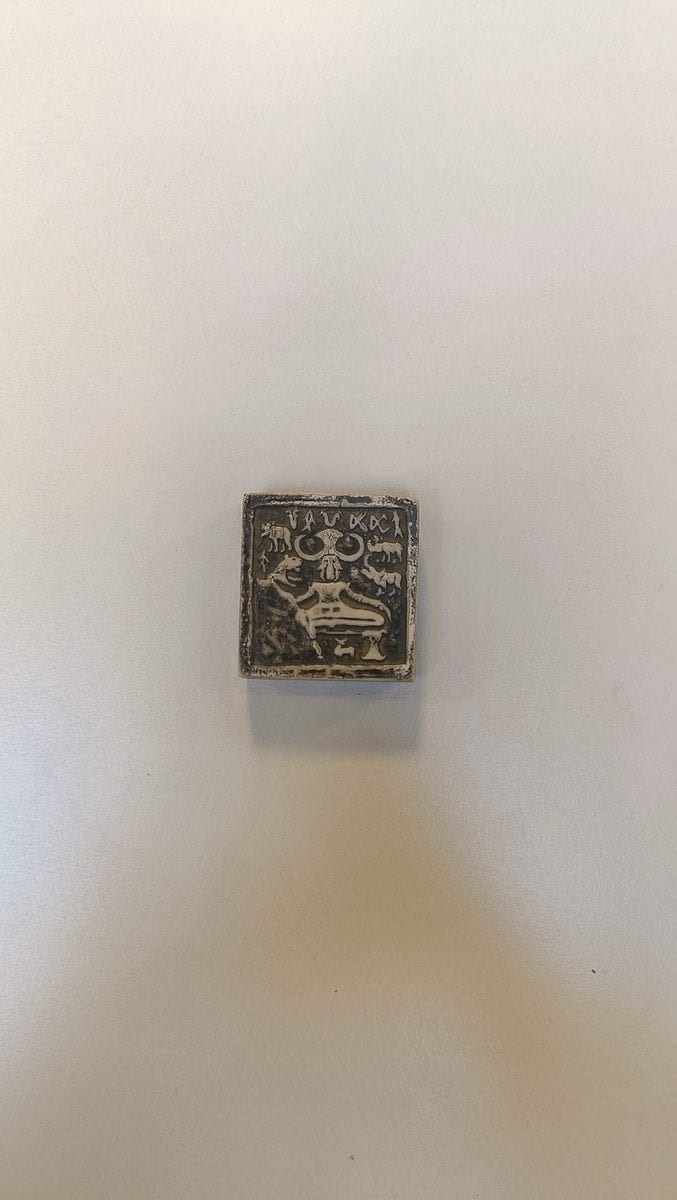 Photograph of the Pashupati seal, a small square Indus Valley steatite seal showing a seated horned figure surrounded by animals, with a row of Indus script signs across the top edge.