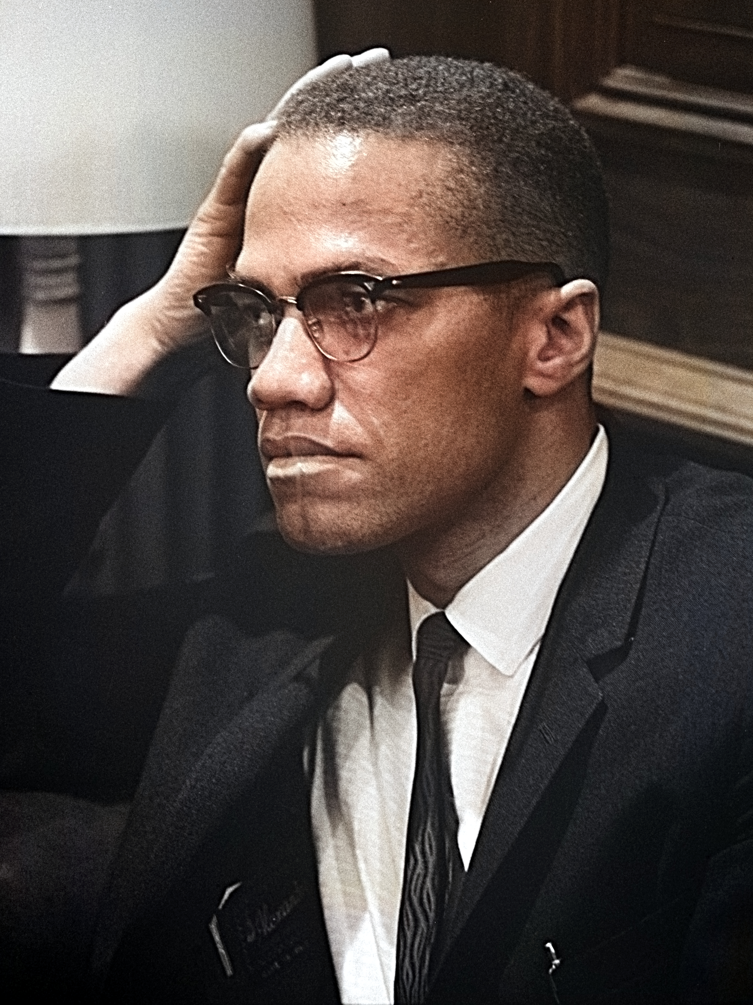 Black-and-white head-and-shoulders portrait of Malcolm X in 1964, wearing a suit and glasses