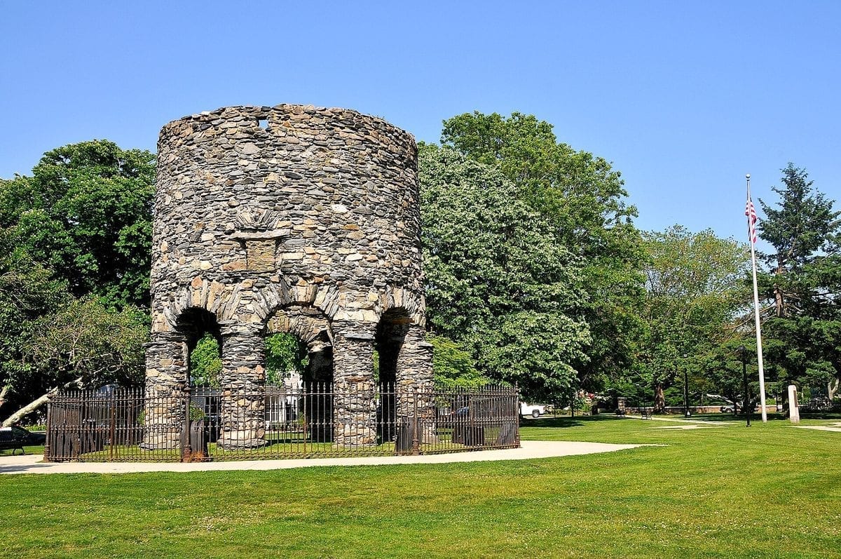 A round, roofless stone tower standing on eight arched columns in a grassy park, the Newport Tower in Newport, Rhode Island.