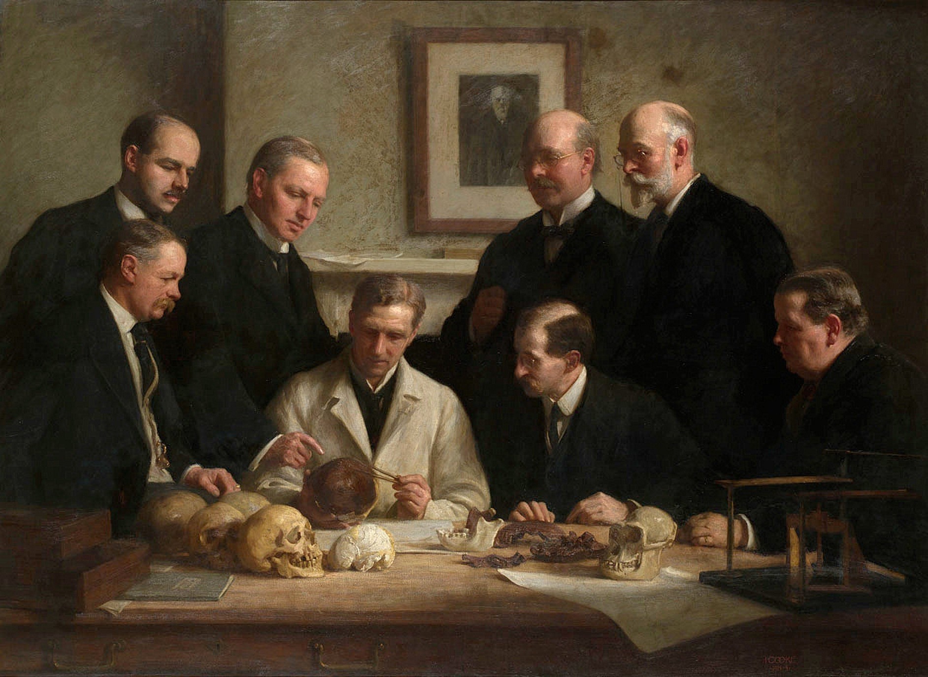 John Cooke's 1915 group portrait showing scientists in suits gathered around a table examining the Piltdown skull.