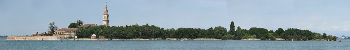 Wide panoramic view across the water of the small, tree-covered island of Poveglia in the Venetian lagoon, with its low buildings and bell tower visible, seen from the Lido.