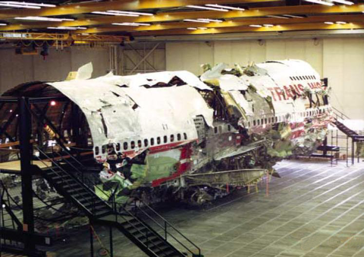 The reconstructed fuselage of TWA Flight 800, its recovered wreckage reassembled on a steel frame inside an NTSB hangar